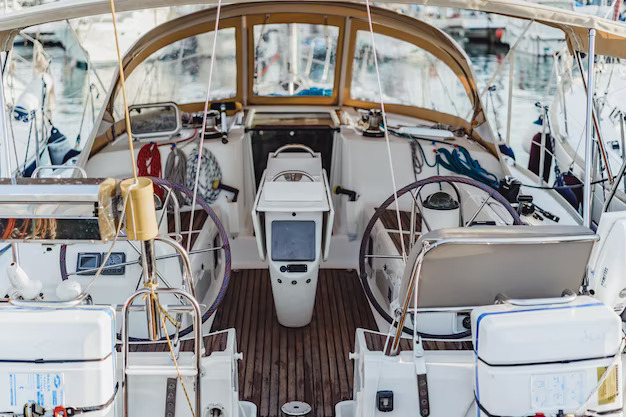 A sailboat cockpit docked in a marina. The cockpit is open and spacious, with a comfortable seating area and a steering wheel.